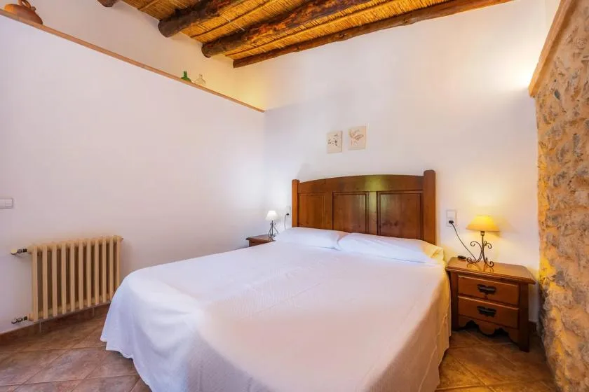 A bedroom with a neatly made bed beneath exposed wooden ceiling beams.