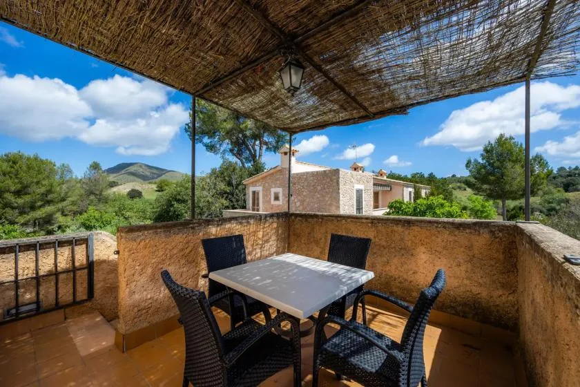 A shaded outdoor dining area overlooks a stone house and green hills.