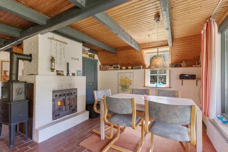 A dining area with a table and chairs beside a tiled stove.