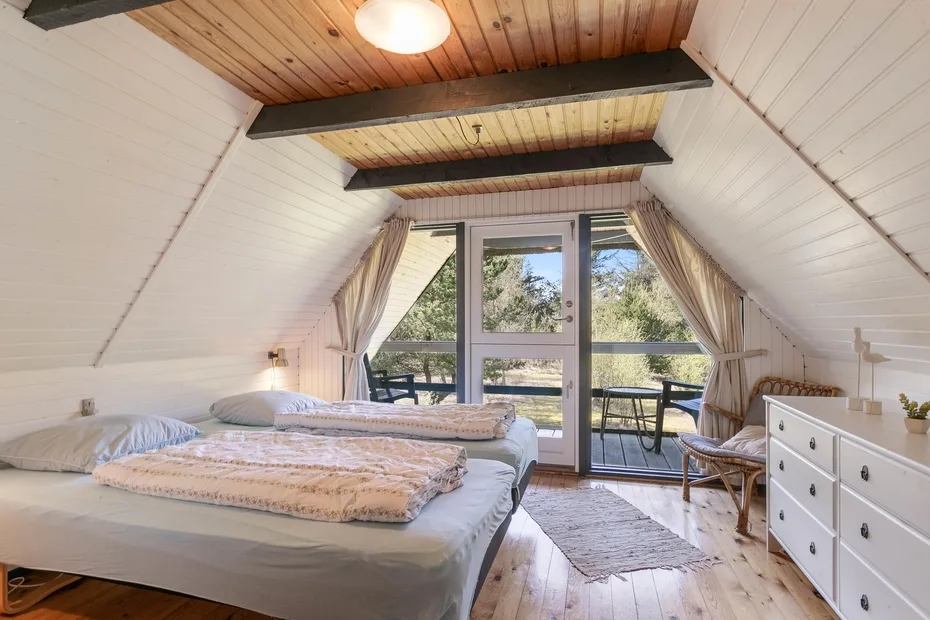 A bright bedroom with two beds and glass doors opening onto a balcony.