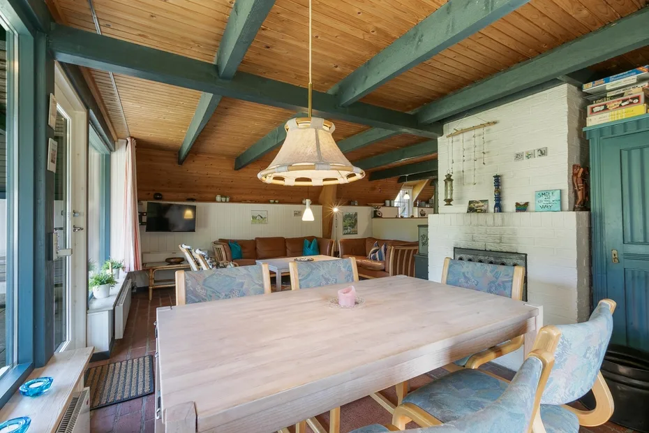 A dining room with a large table beneath exposed beams and a hanging light.