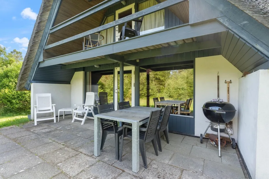 An outdoor patio has a dining table and chairs beside a barbecue grill.