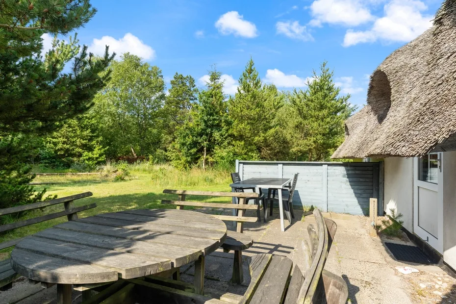 An outdoor seating area with a round wooden table beside a thatched-roof building.