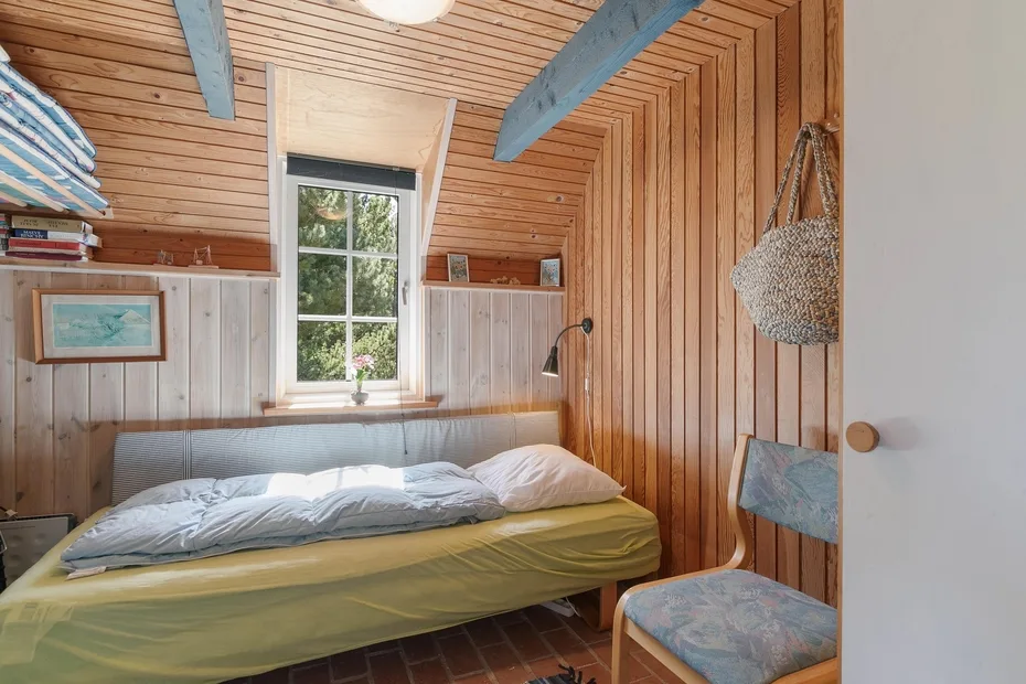 A compact bedroom with a bed beneath a window and wood-paneled walls.