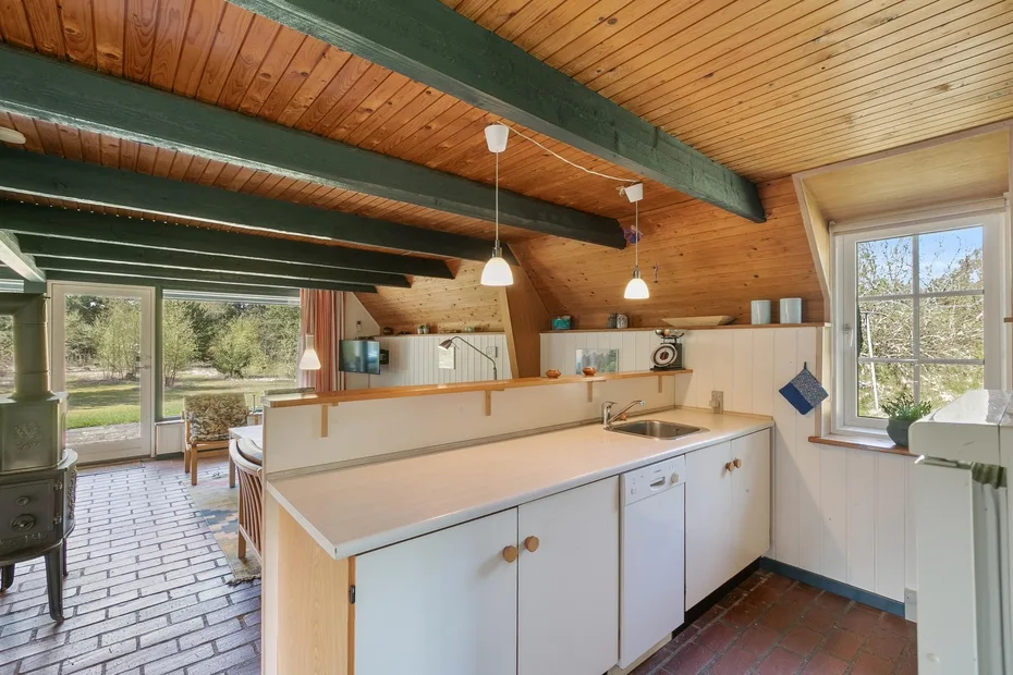 A bright kitchen with a long counter, pendant lights, and large windows.