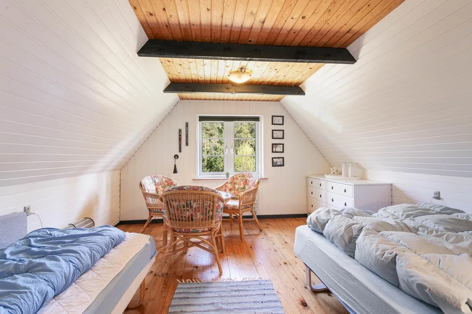 A bright attic bedroom with beds, a window, and a small seating area.