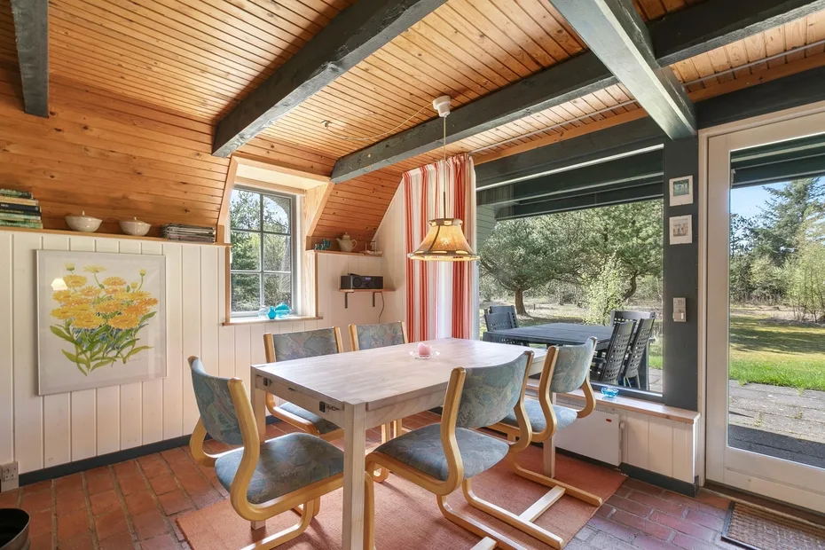 A dining area with a wooden table beside large windows overlooking trees.