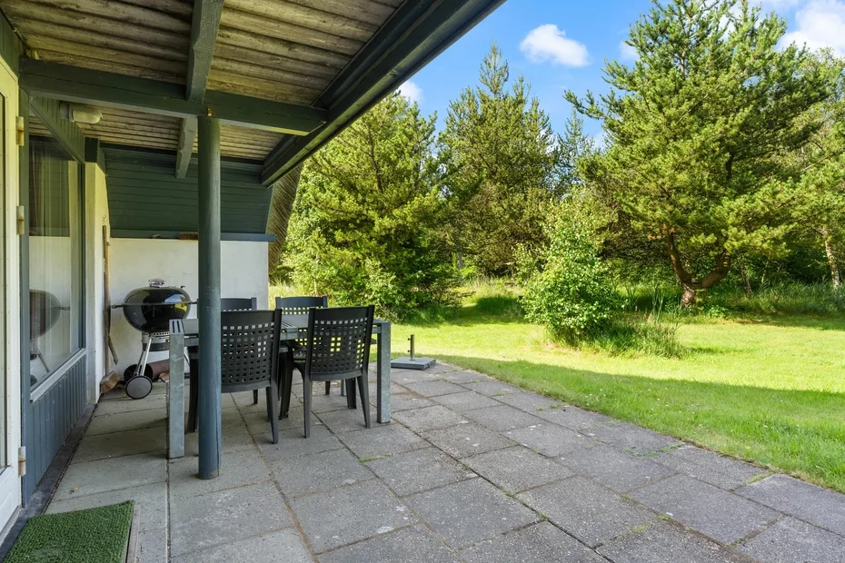 A covered patio with outdoor seating overlooks a grassy garden and trees.