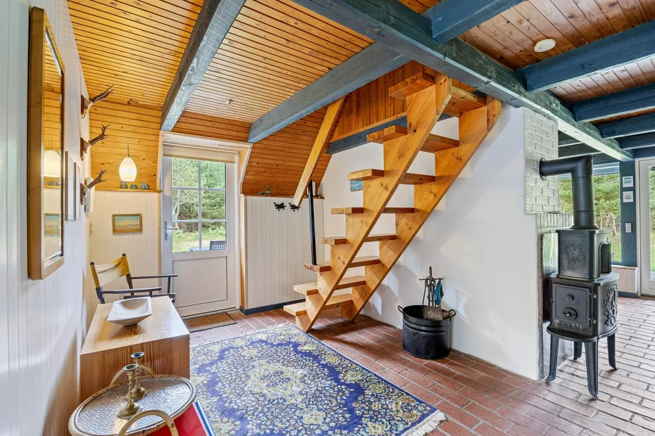 A bright room with a wooden staircase, patterned rug, and black stove.