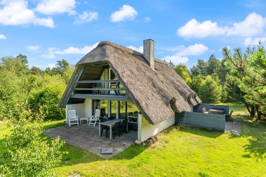 A thatched-roof cottage with an outdoor patio surrounded by greenery.