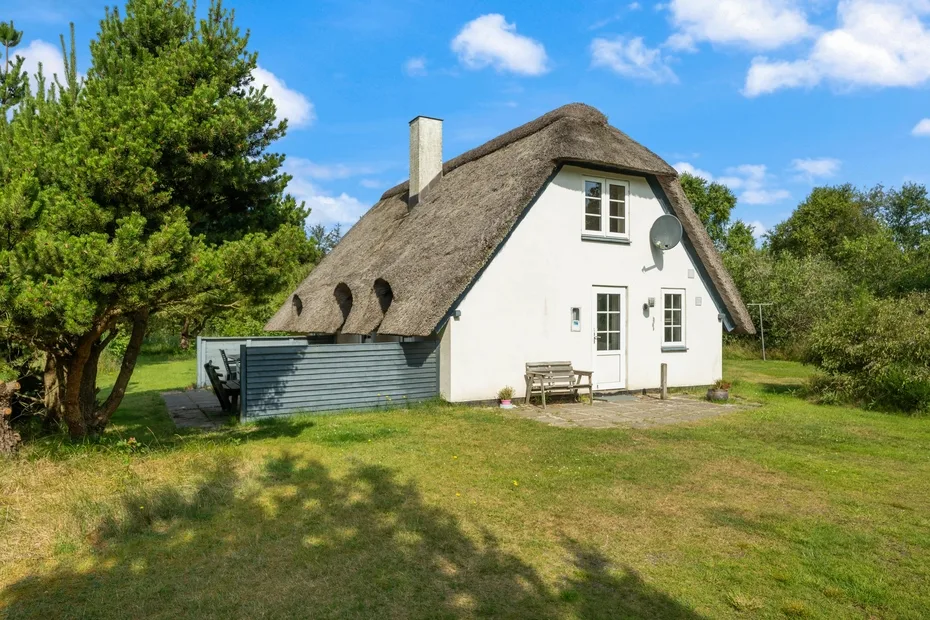 A white cottage with a steep thatched roof stands in a grassy yard.