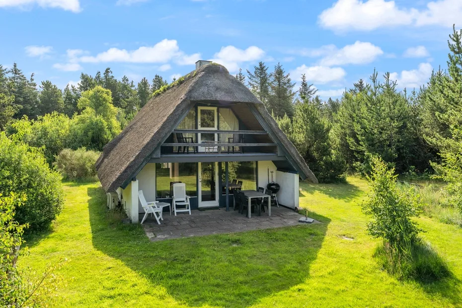 A thatched-roof cabin with a small patio sits in a grassy clearing.