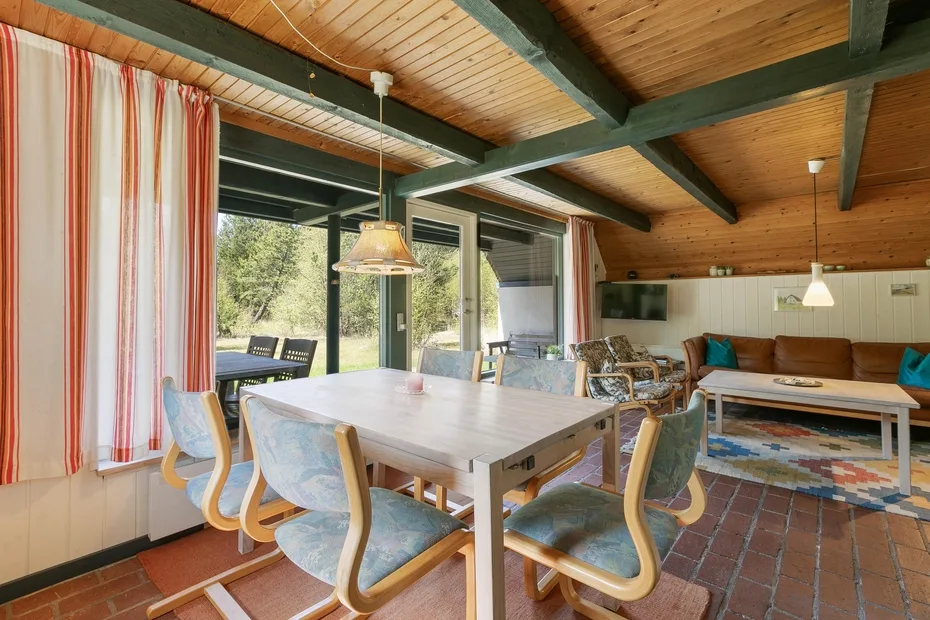 A dining and living area with a large table, seating, and wood-paneled ceiling.
