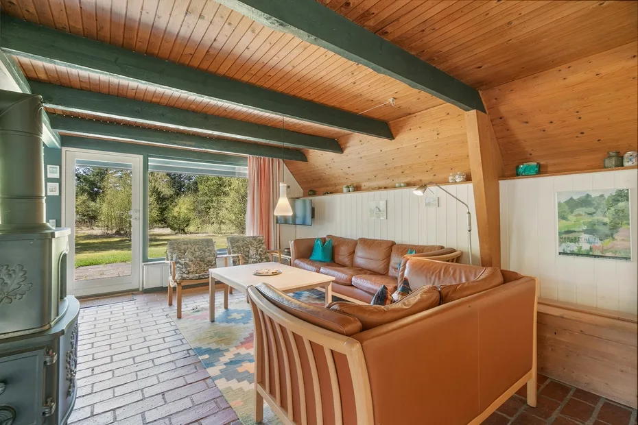 Una sala de estar con asientos de cuero, techo revestido de madera y grandes ventanas.