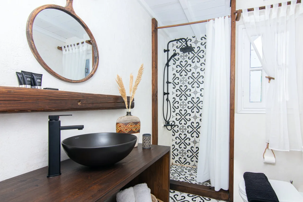 Un baño luminoso con una encimera oscura, un lavabo sobrepuesto y una zona de ducha estampada.