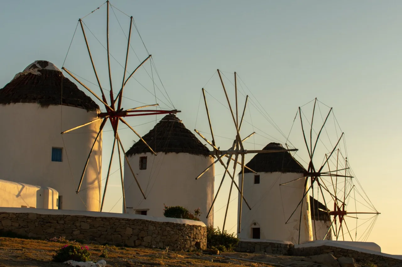 Molinos blancos tradicionales se alzan en una ladera bajo la luz cálida del atardecer.
