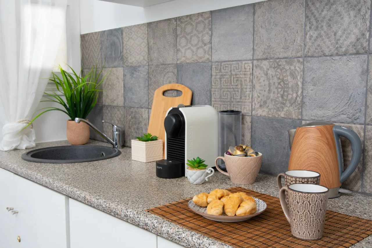 Una encimera de cocina con cafetera, tazas y bollería.