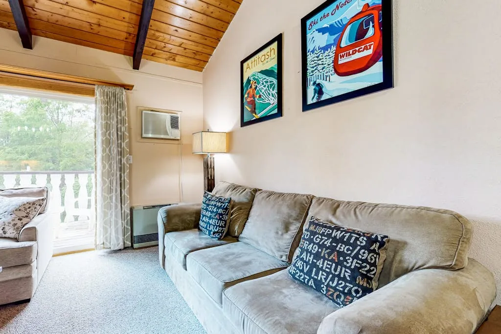 A living room with a long sofa, framed posters, and a wood-paneled ceiling.