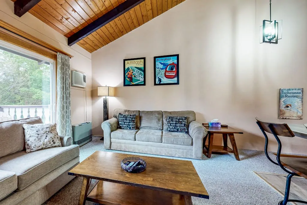 A living room with seating, a wooden coffee table, and a vaulted wood ceiling.