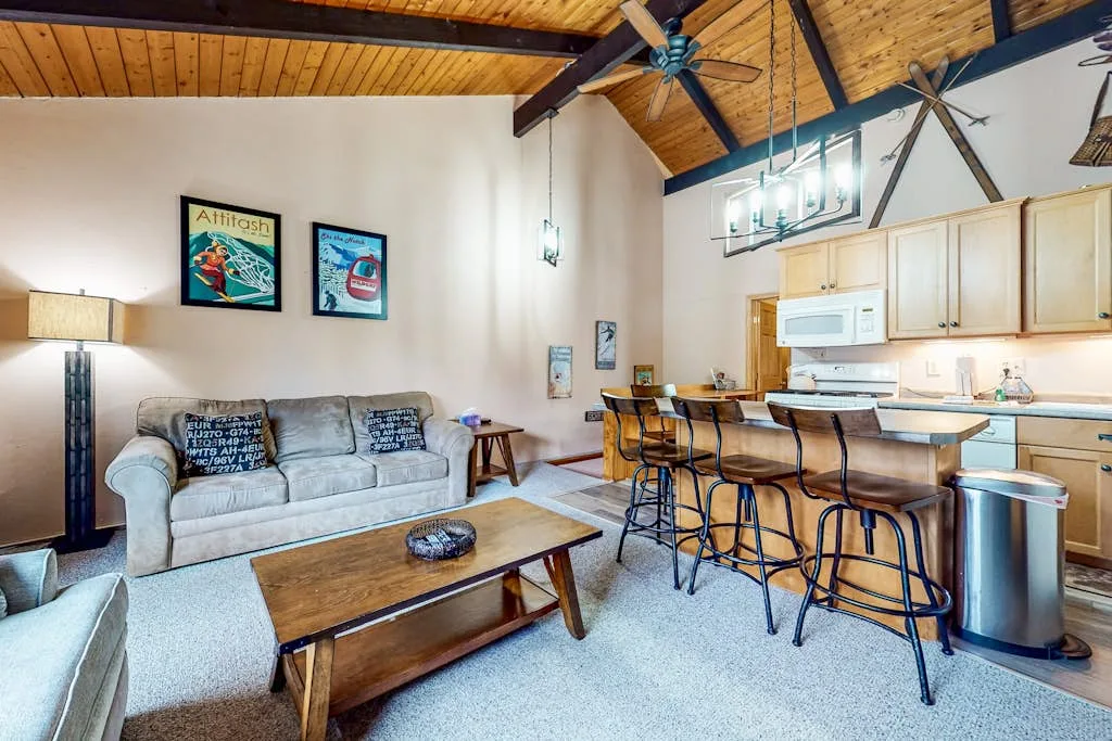 A living area with a sofa and coffee table opens into a kitchen with a breakfast bar.