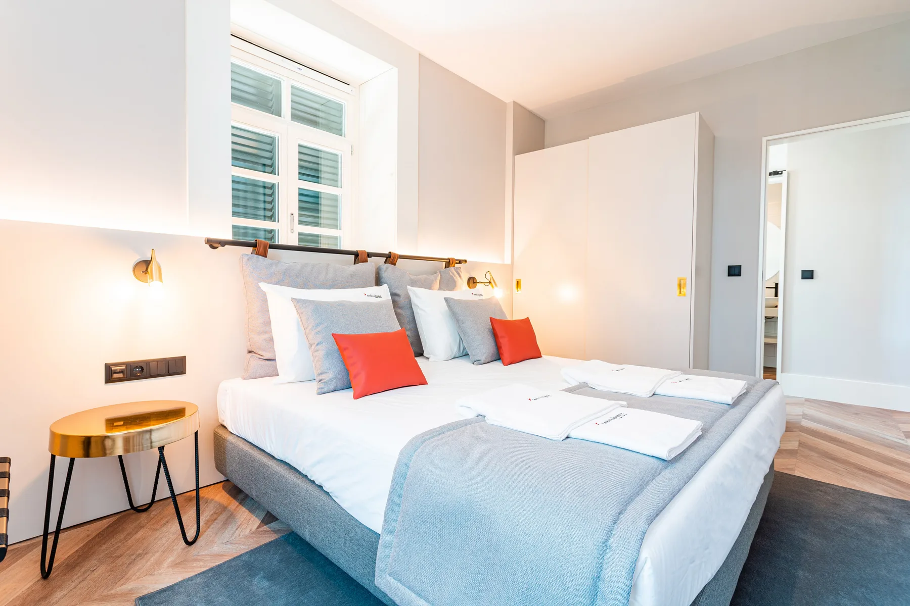 Un dormitorio luminoso con una cama bien tendida y una ventana sobre el cabecero.