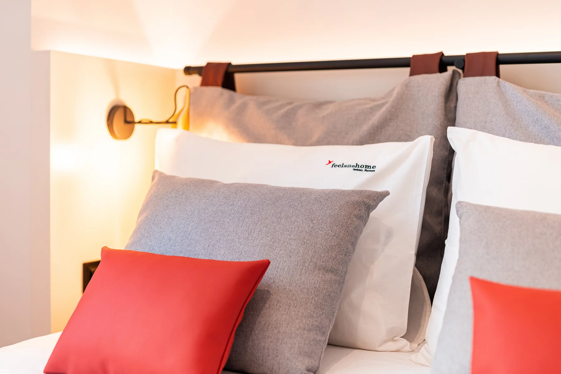 Un dormitorio con almohadas sobre una cama junto a una lámpara de pared encendida.