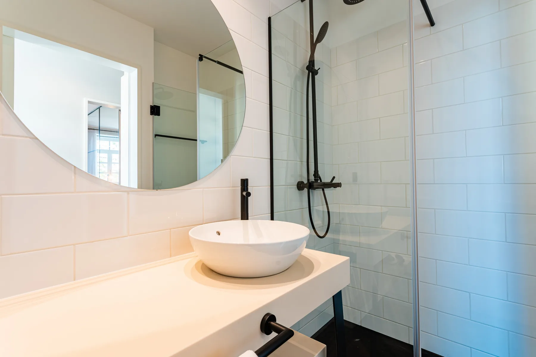 Un lavabo de baño con un espejo redondo junto a una ducha con azulejos.