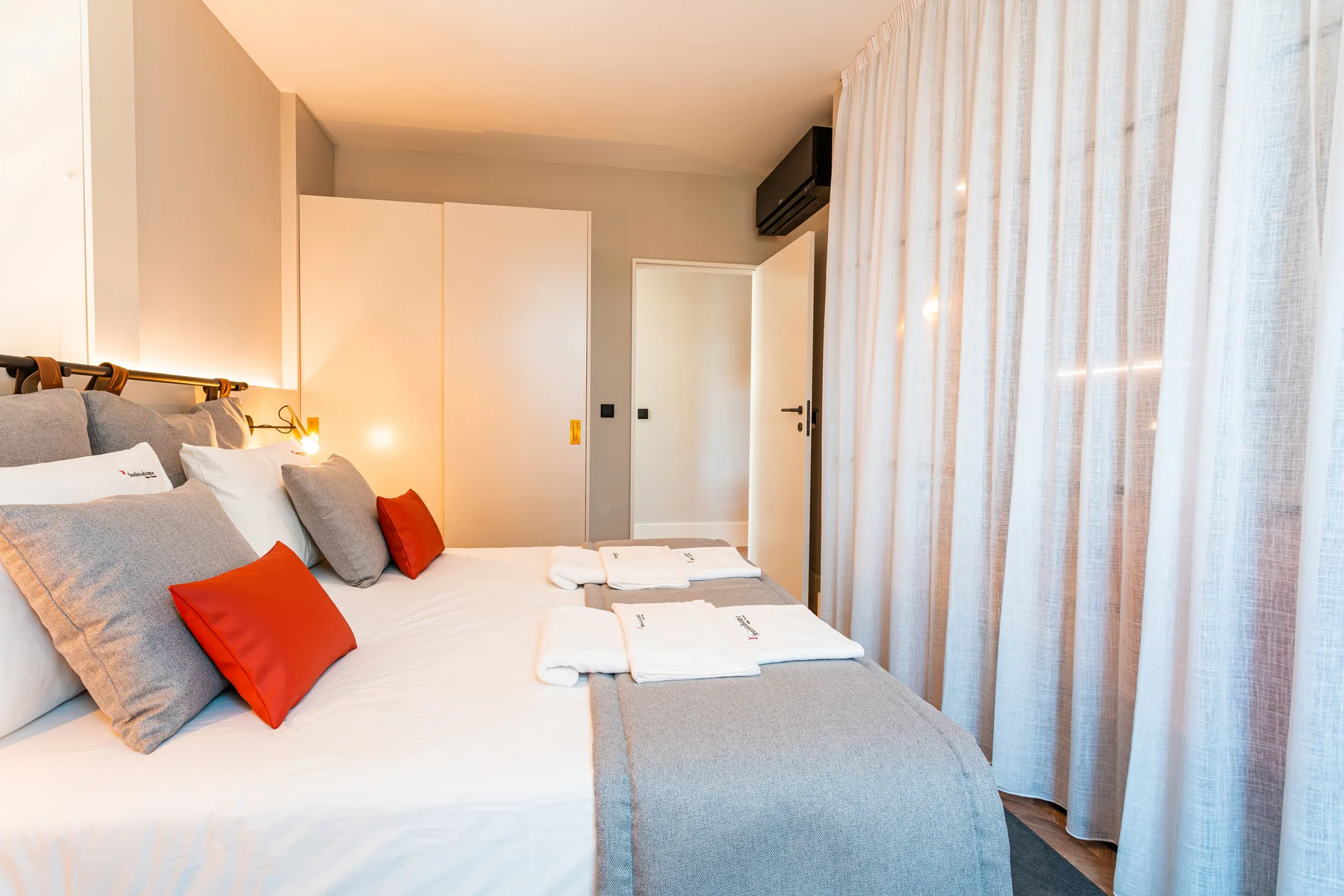 Un dormitorio con camas arregladas y cortinas translúcidas junto a la ventana.