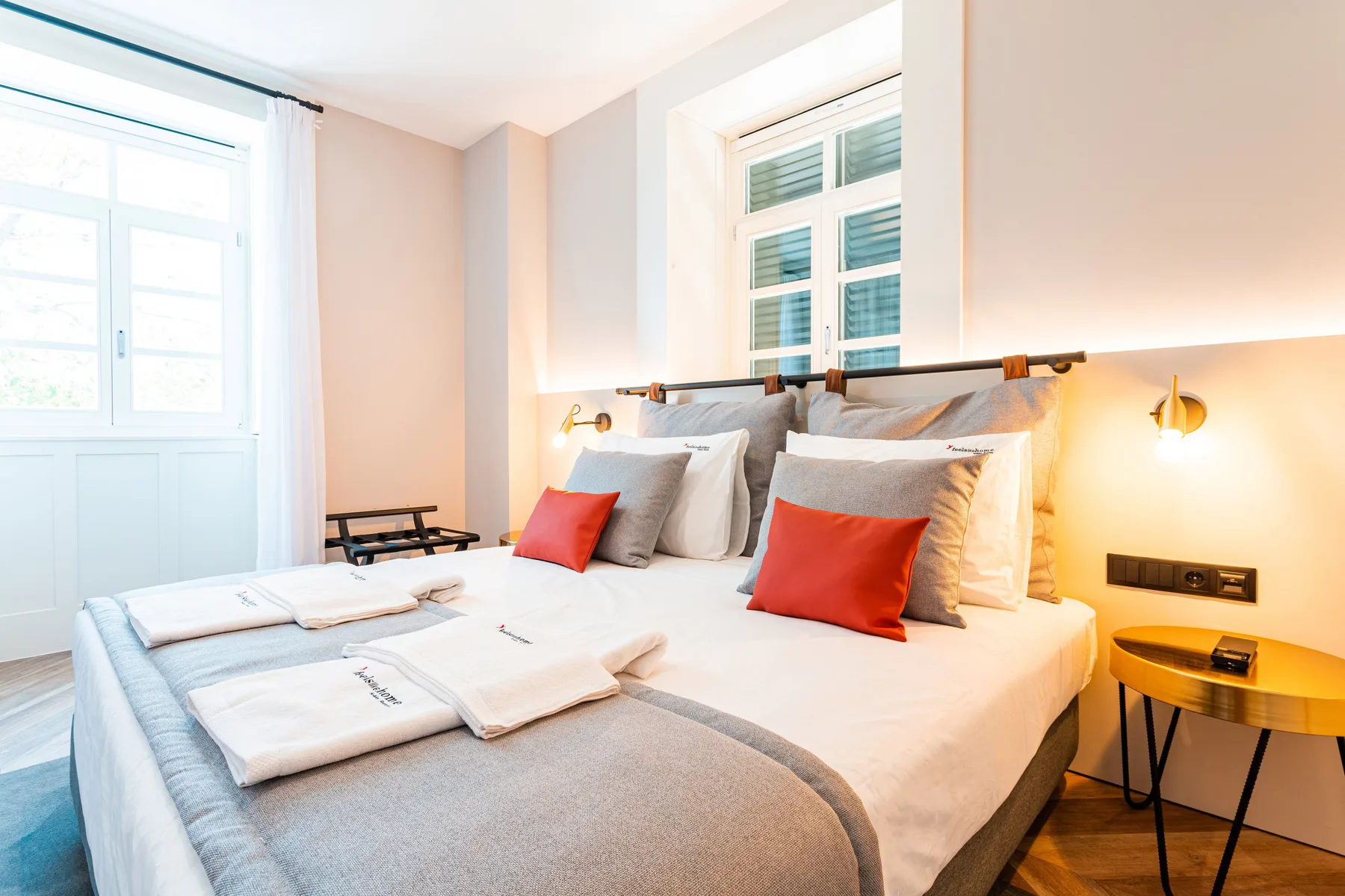 Un dormitorio luminoso con dos camas, ropa de cama blanca y cojines rojos.