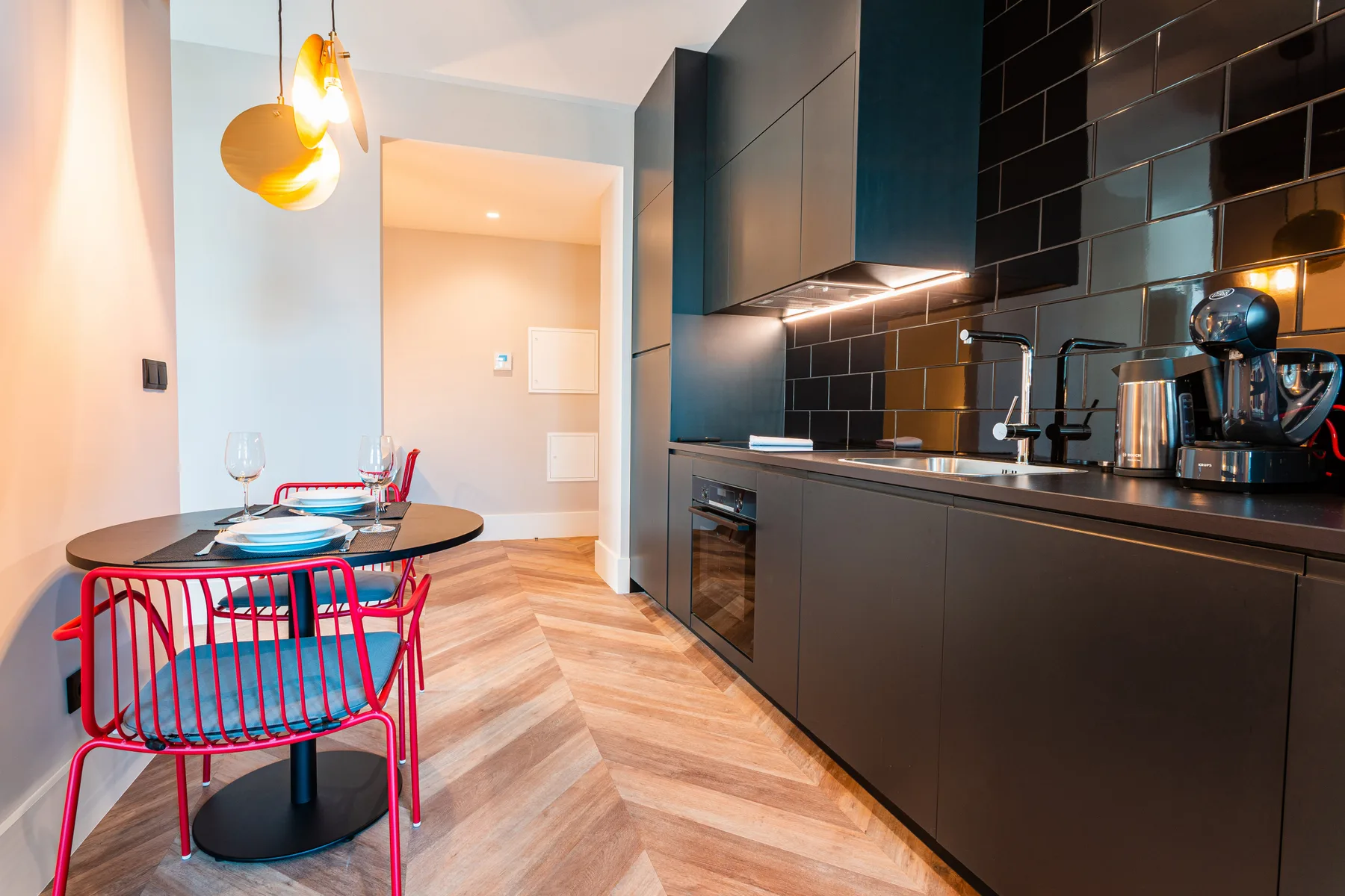 Comedor junto a una cocina moderna con muebles oscuros y un salpicadero de azulejos negros.