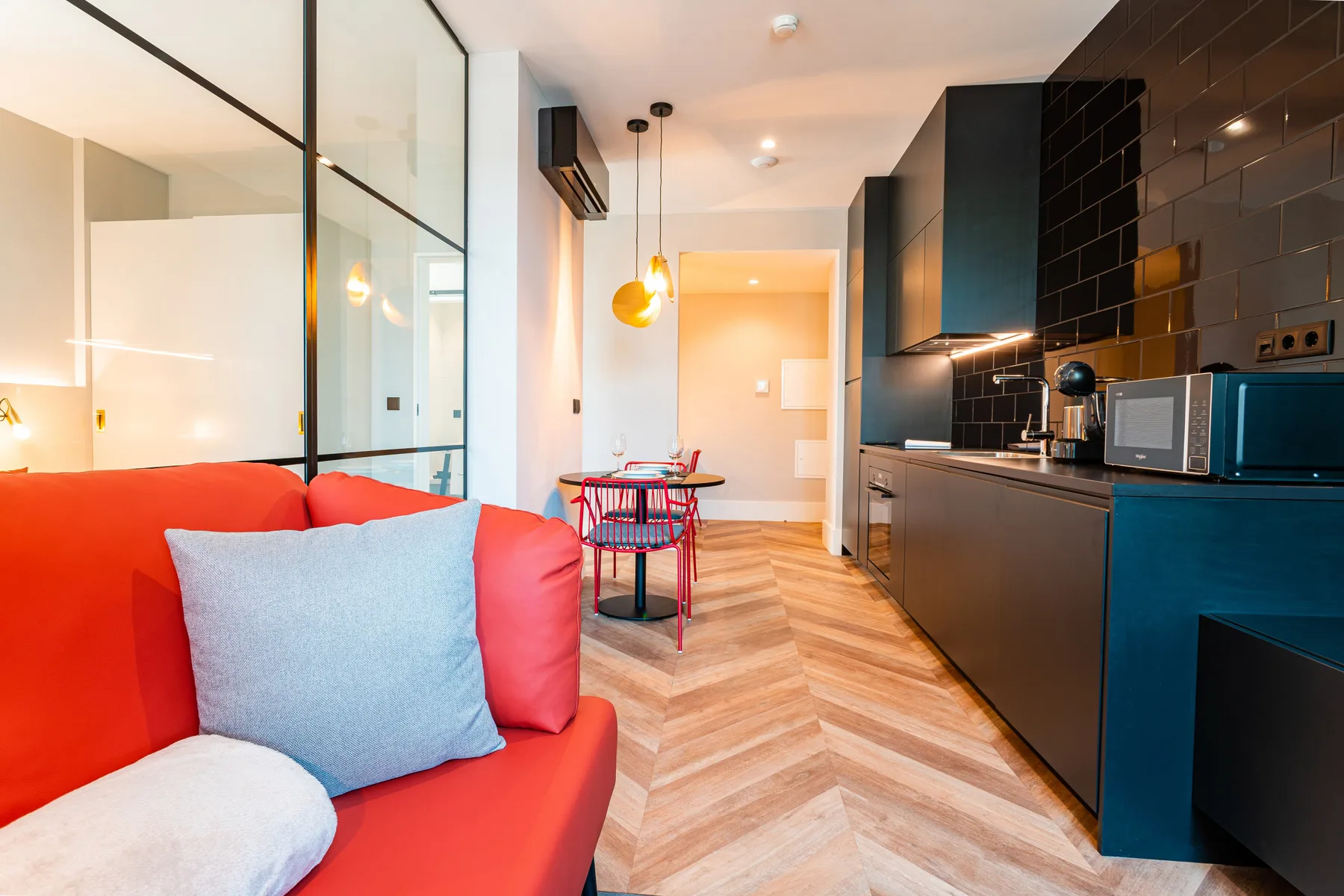 Una sala de estar con asientos coloridos junto a una cocina compacta y una mesa de comedor.