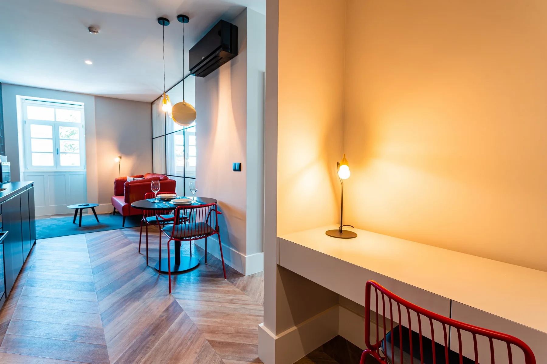 An open-plan living and dining area with a table, seating, and a lit desk nook.