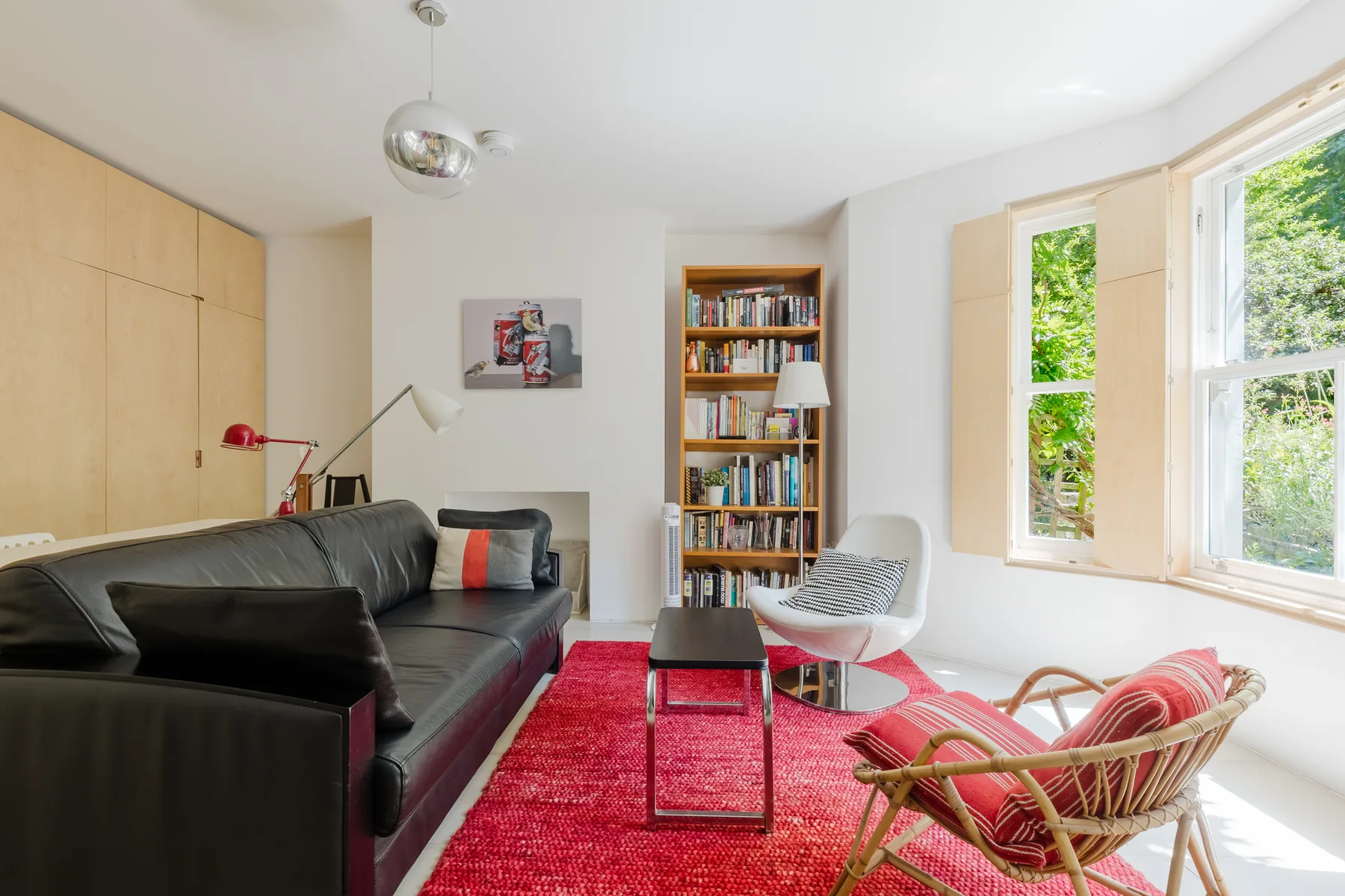 Una sala luminosa con asientos, una estantería y ventanas grandes.