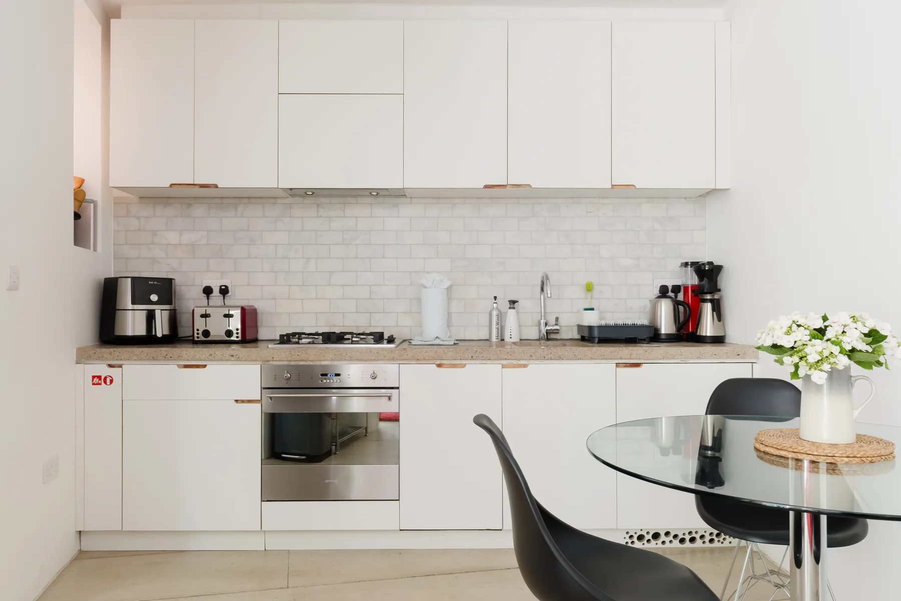 A bright kitchen with white cabinets and a glass dining table.