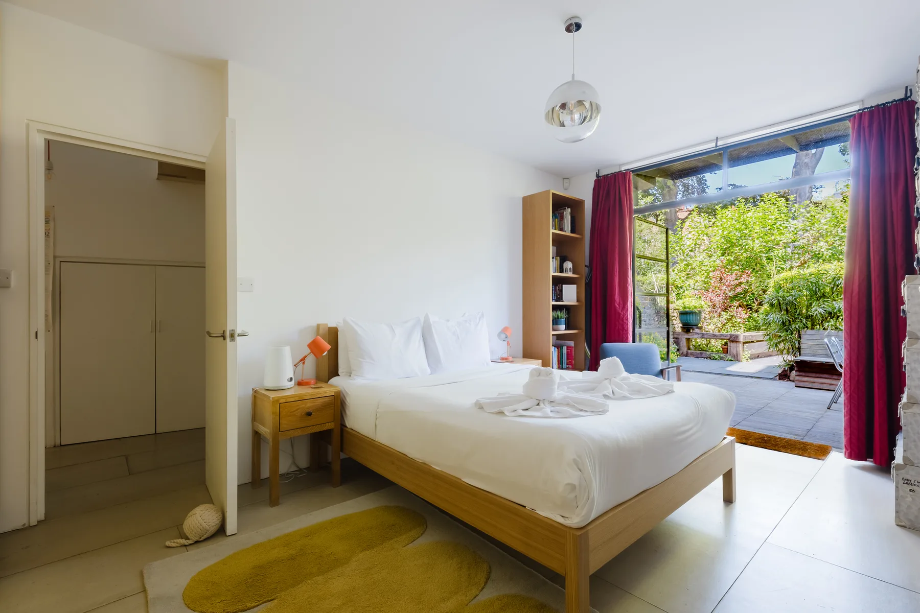 Un dormitorio con una cama bien hecha junto a una gran ventana con vistas a la vegetación.