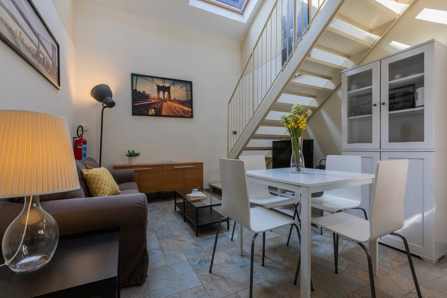 A bright living and dining area has a table beneath an open staircase.
