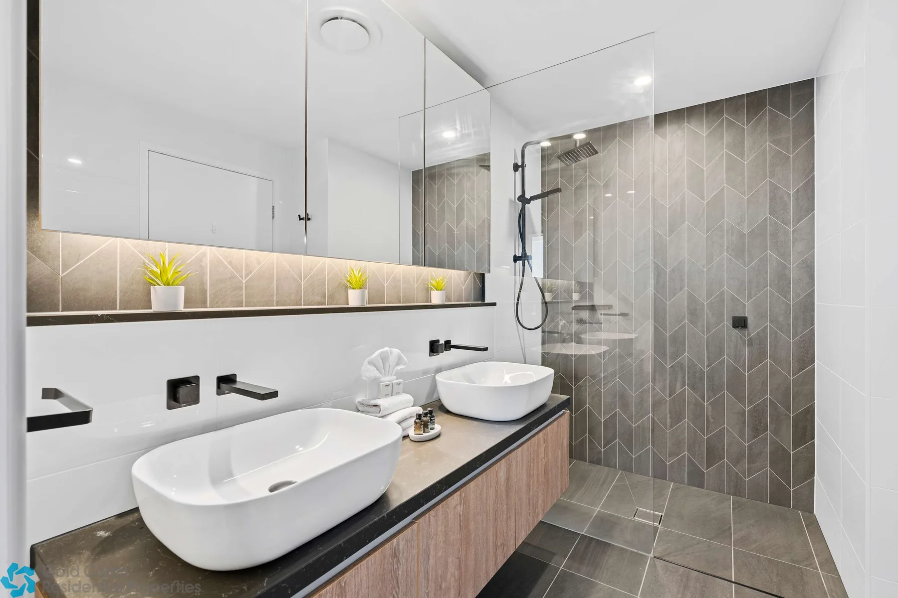 Baño moderno con dos lavabos blancos sobre encimera y una ducha alicatada.