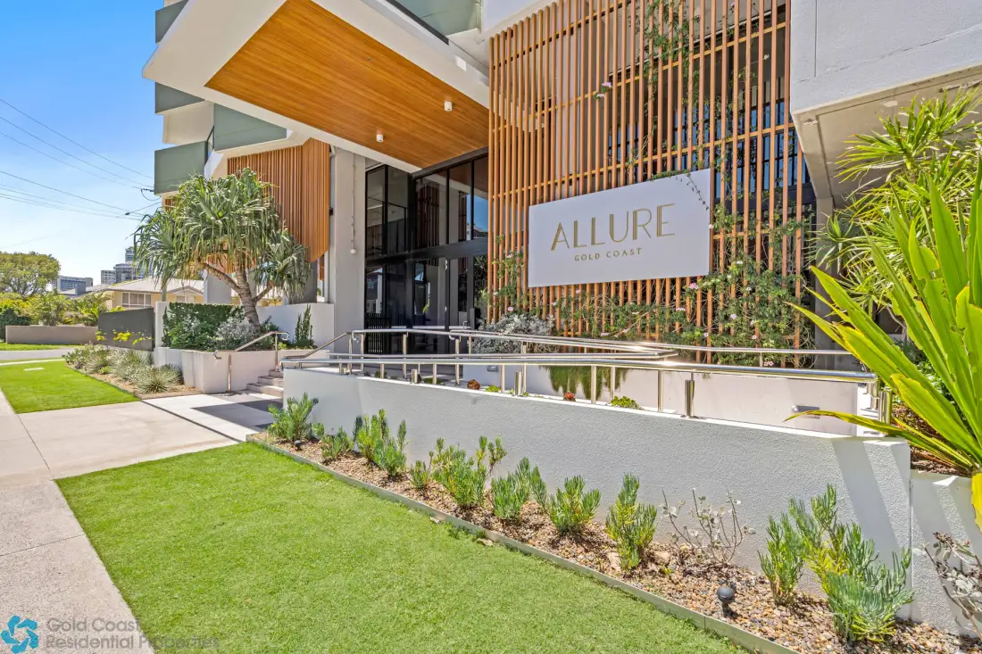 La entrada de un edificio moderno está enmarcada por listones verticales y vegetación.