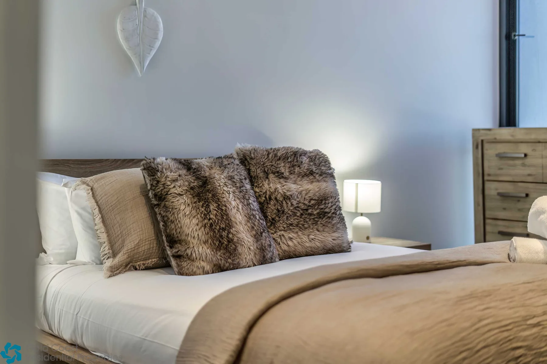Un dormitorio con varios cojines, una lámpara de noche y una cómoda de madera.