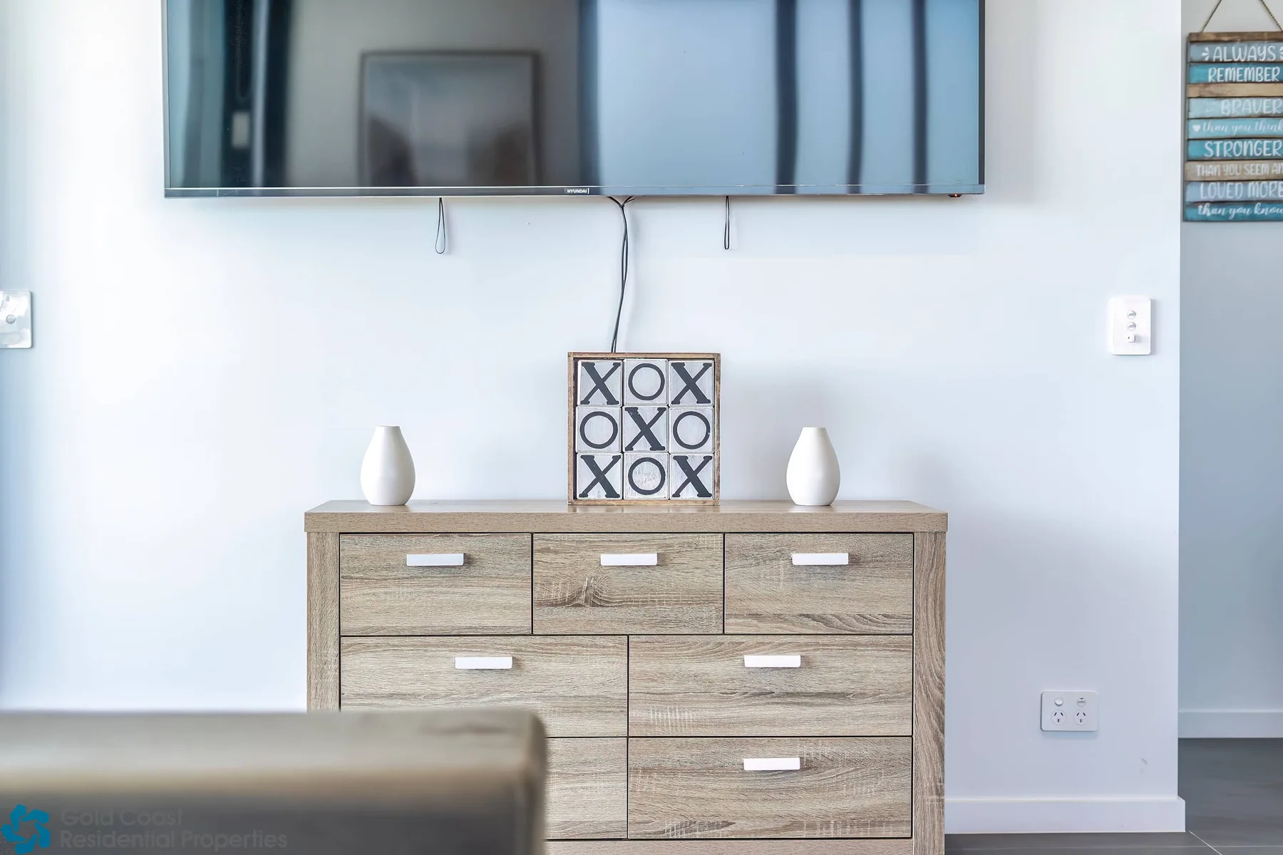 Un televisor cuelga sobre una cómoda de madera con un cuadro y jarrones decorativos.