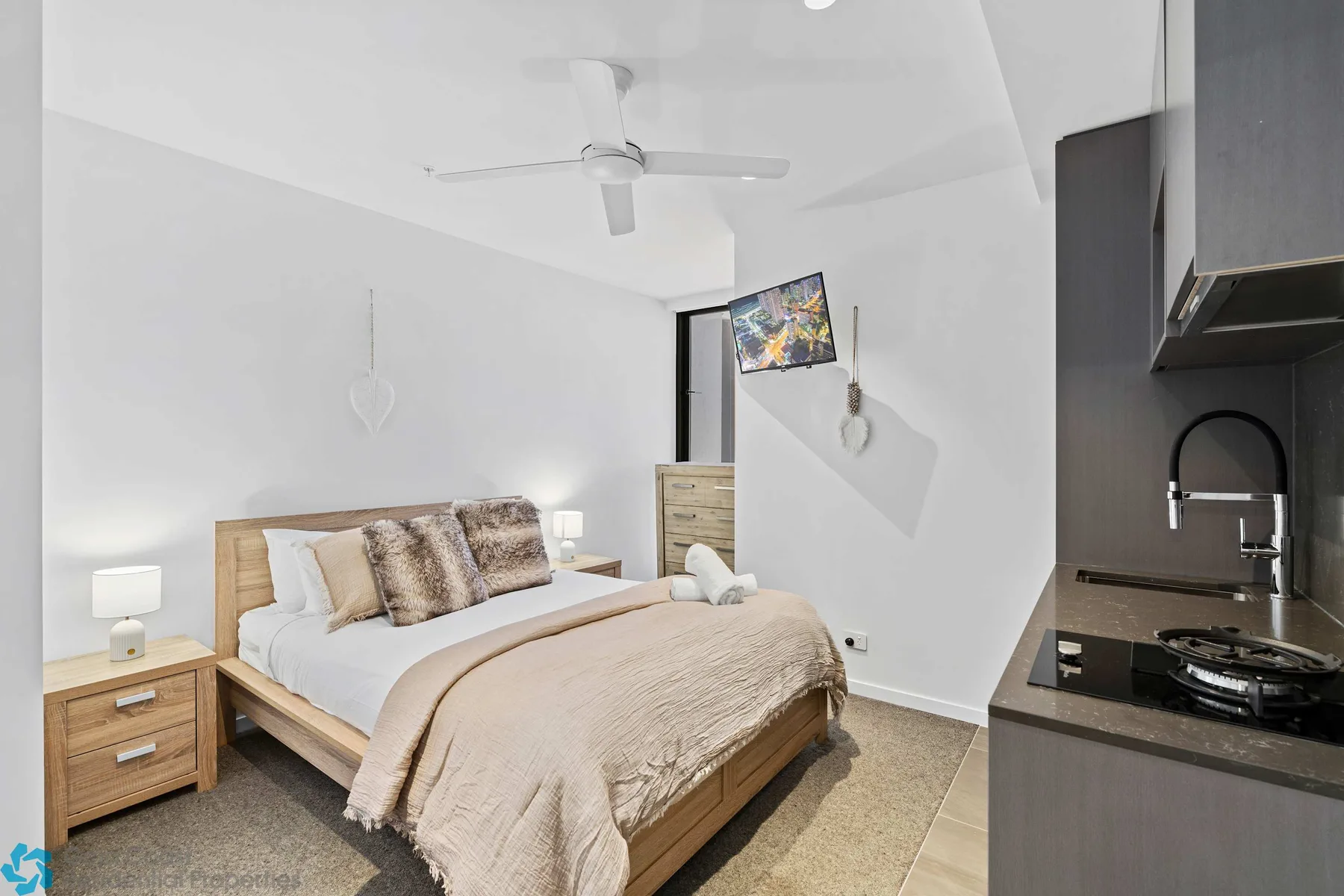 Un dormitorio con una cama bien arreglada y una pequeña cocina junto a la pared derecha.