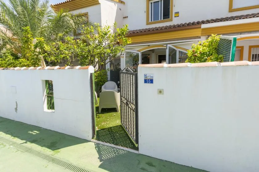A white house stands behind a low wall and an open metal gate.