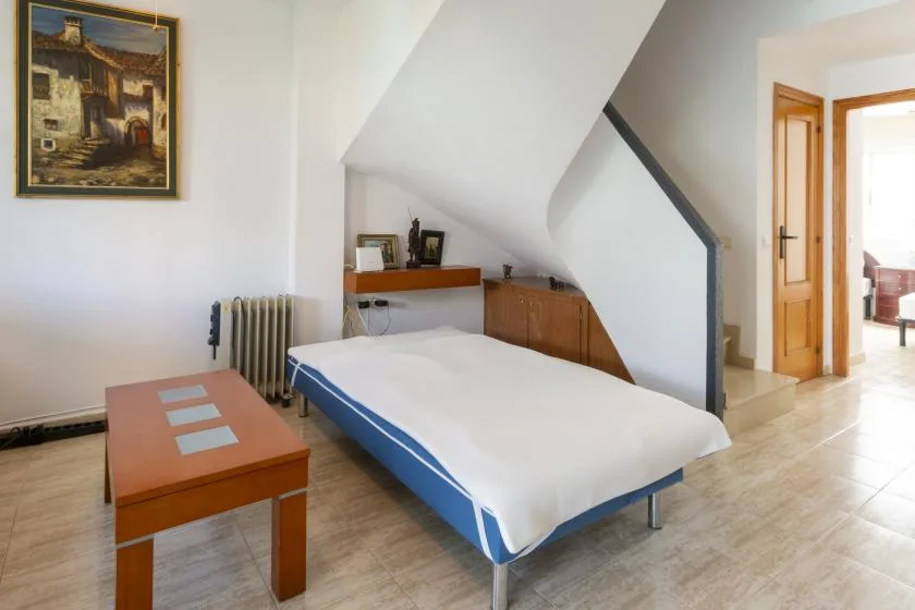 A bedroom with a bed beneath a sloped ceiling and a wooden bedside cabinet.