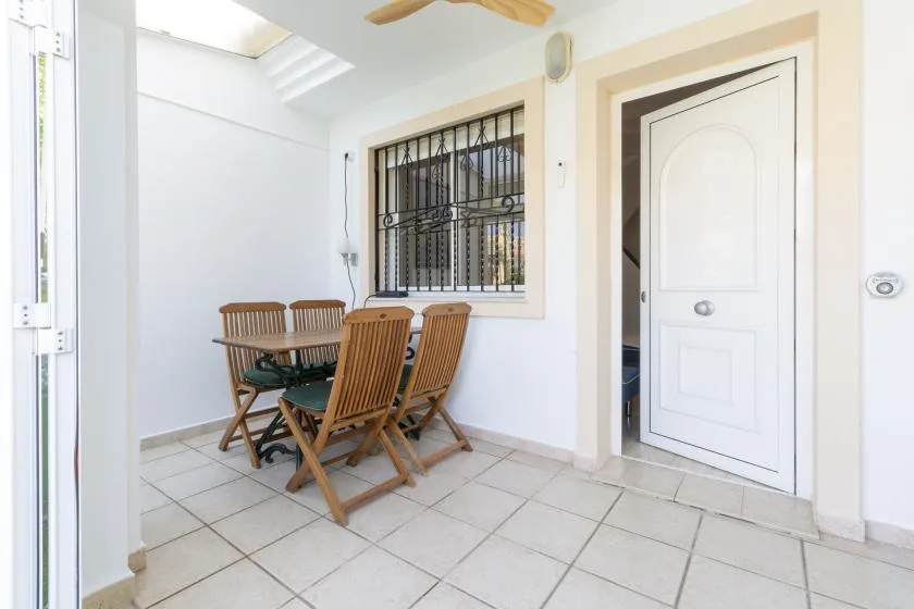 A bright tiled patio with a wooden dining table and chairs beside a white door.