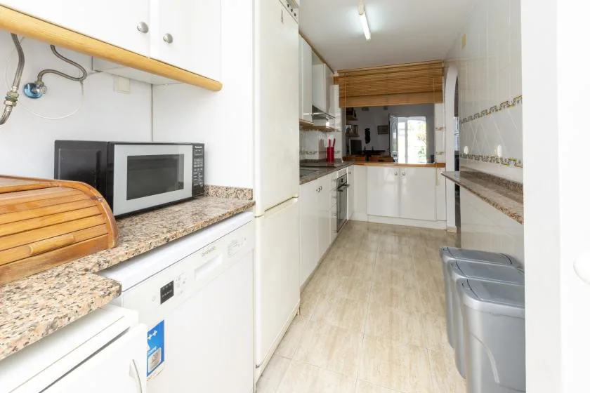 A narrow kitchen with white cabinets, countertop appliances, and a washing machine.