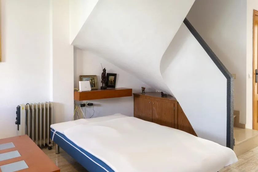A bedroom with a bed beneath a sloped ceiling and wooden cabinets.