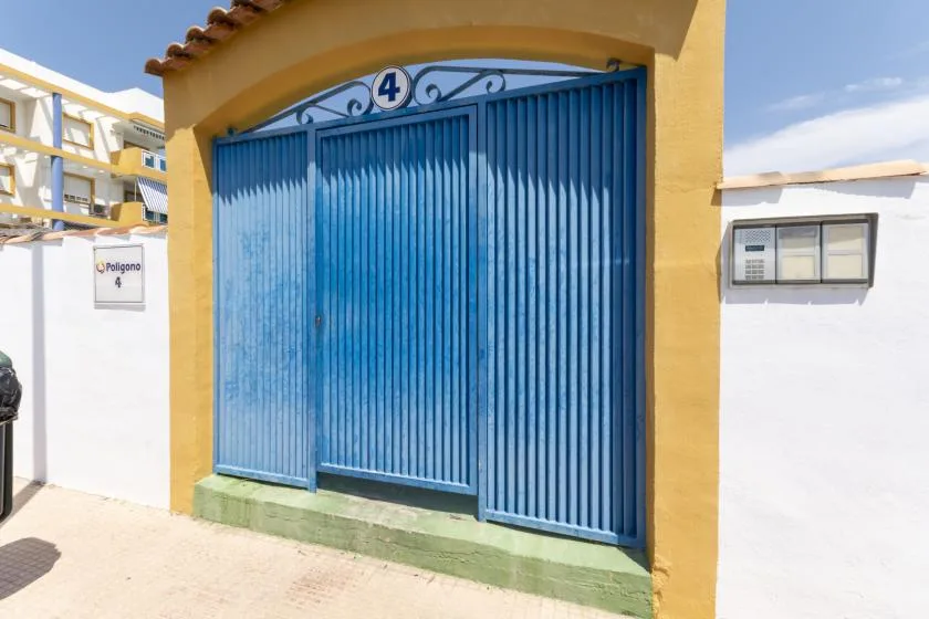 A blue metal gate is set into a yellow entrance wall.