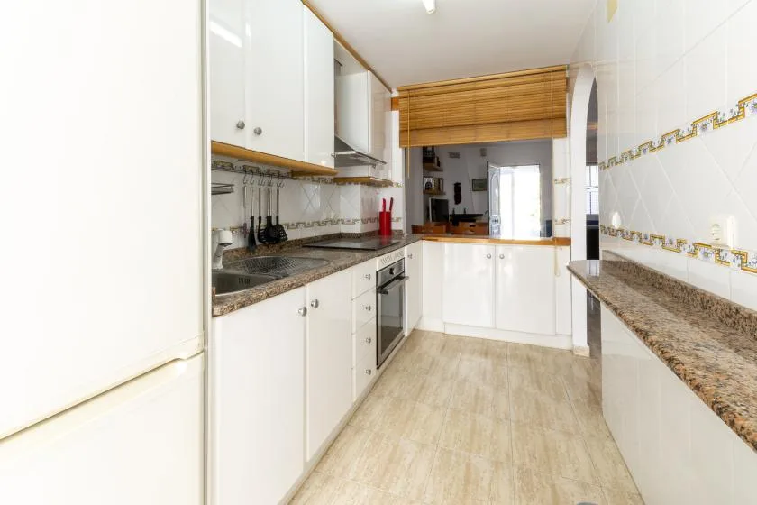 A bright kitchen with white cabinets, long counters, and a serving opening.