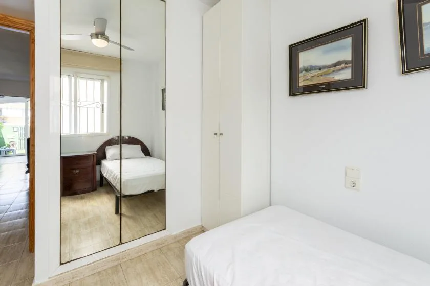 A bright bedroom with a white bed, mirrored wardrobe, and framed pictures.