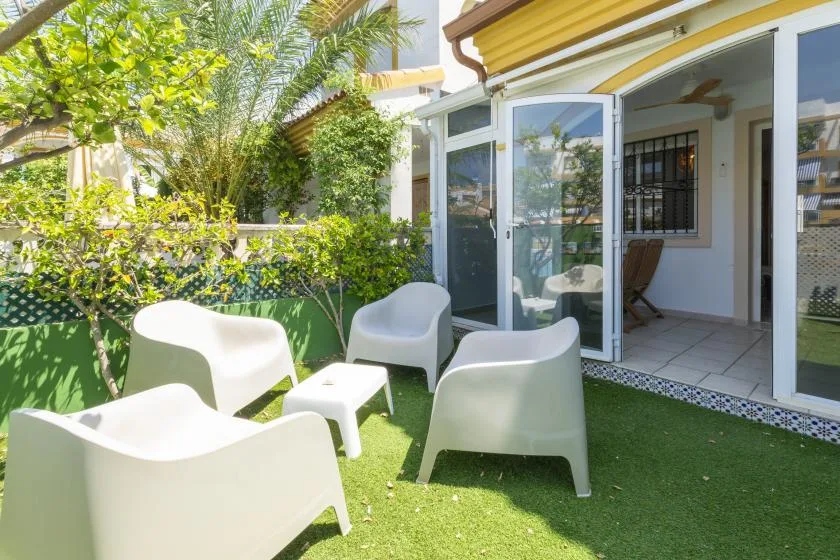 A patio seating area with white chairs on artificial grass beside an open doorway.